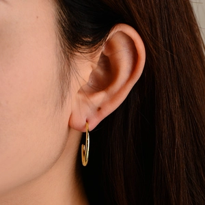 Close-up of polished gold C-shape hoop earrings worn by a model in a natural setting