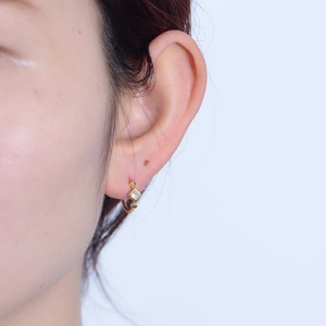 Close-up of a gold s925 silver hoop earring with a square zircon on a model ear