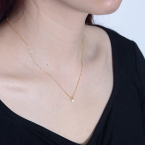 Golden heart necklace with zircon stone shown on model with dark clothing background