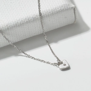 Minimalist sterling silver heart necklace with a sparkling center zircon on white stone
