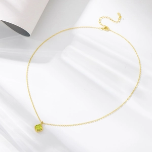 Detail of square green zircon pendant with gold bead edge and fine chain on white fabric