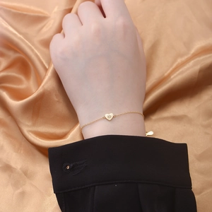 Macro detail of a 14K gold heart bracelet with a star-engraved zircon pendant
