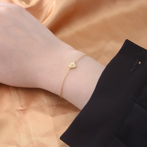 Detail of 14K gold plated heart bracelet with starburst engraving and zircon on a model