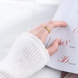 Minimalist gold chain link ring worn on index finger over white knit sweater background