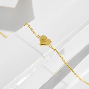 Detail of 14K gold plated silver heart bracelet with starburst engraving and zircon stone