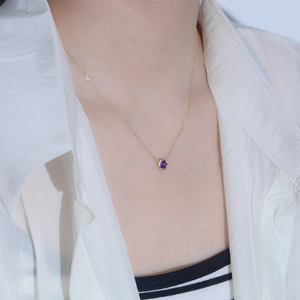 Macro detail of a hexagonal purple gemstone pendant necklace on a gold chain
