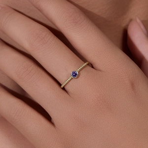Elegant gold twisted band ring with a round purple amethyst bezel set on a woman's finger