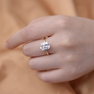 Macro shot of rectangular cut zircon ring with four-prong gold plated band on finger