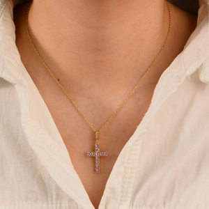 Collier croix doré pour femme orné de zircons violets étincelants en gros plan sur un mannequin