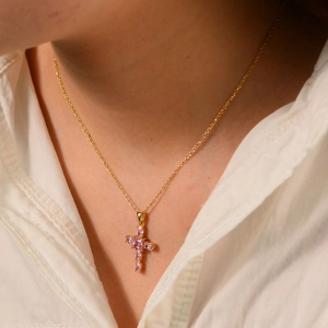 Close-up of a gold cross pendant necklace featuring six pink marquise-cut stones on a model