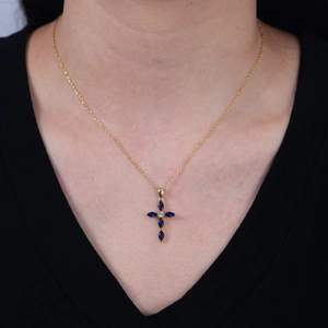 Elegant gold cross necklace with blue marquise crystals worn by a model on a V-neck top