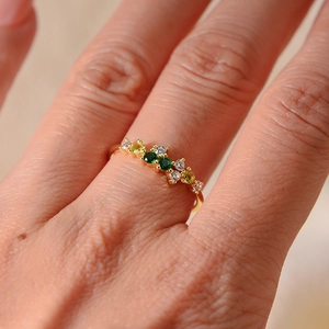 Macro shot of gold band ring featuring colorful round-cut crystal stones on a finger