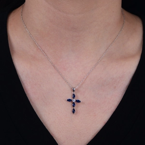 Macro shot of silver cross necklace with four marquise-cut blue zircon stones on skin