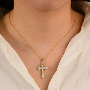 Gold cross pendant necklace with clear crystals worn by a female model on a white shirt