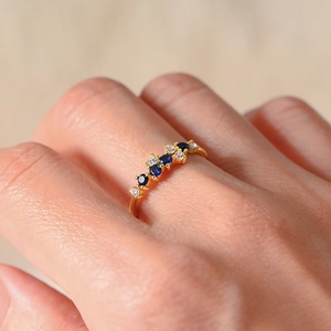 Detailed close-up of a gold ring with alternating blue and white gemstones on a finger