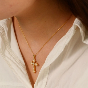 Close-up of gold-plated silver cross necklace with pavé zircons on female model