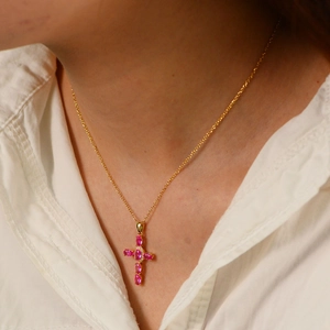 Dettaglio della collana a croce dorata con zirconi rosa indossata da un modello