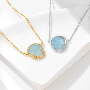 Elegant silver and gold necklaces with oval sea blue gemstone pendants on stone base