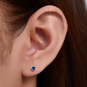 Macro shot of 925 silver heart-shaped blue sapphire stud earring worn on earlobe