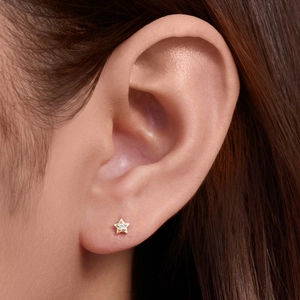 Detailed view of a small gold star-shaped stud earring with a central zircon on an earlobe