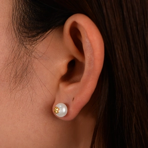 Detailed macro view of a 925 sterling silver pearl stud earring with golden clover charm