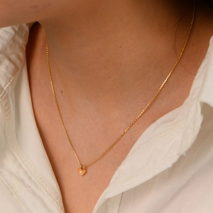 Détail du collier pendentif cœur doré avec zircon sur un col de chemise blanc