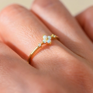 Macro view of opal four-leaf clover flower ring with gold band and side crystals