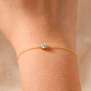 Macro shot of minimalist gold silver bracelet featuring a four-prong set round zircon