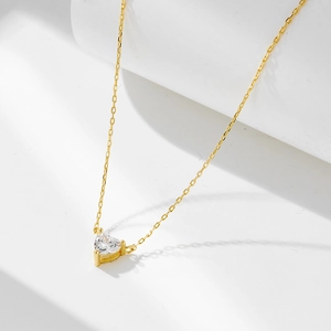 Close-up of golden heart-shaped pendant necklace with three-prong set clear zircon stone