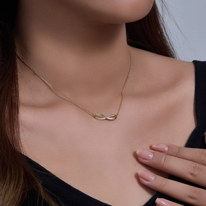 Close-up of a gold infinity necklace with pavé zircons worn by a model on the collarbone