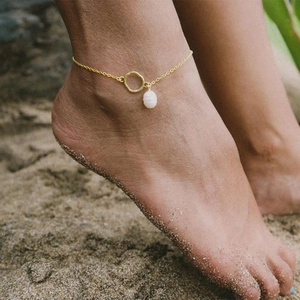 Minimalist gold anklet with irregular circle and pearl pendant on a beach background