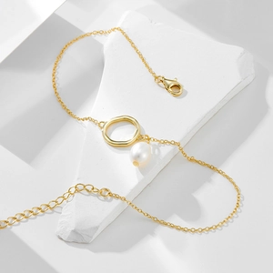 Gold anklet with irregular ring and natural pearl charm on a minimalist geometric stone