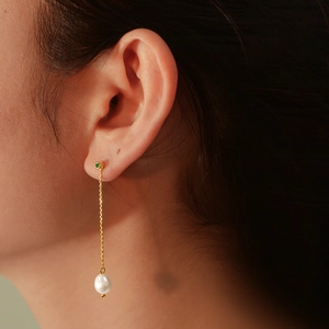 Elegant gold long chain earrings featuring a green gemstone and a white pearl drop on model