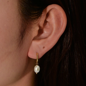 Close-up of elegant gold hoop earring with a white pearl on a model's ear