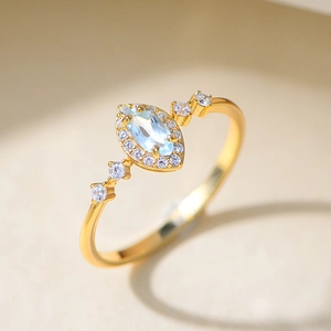 Gold marquise-cut sky blue topaz ring with halo diamonds on a textured white surface