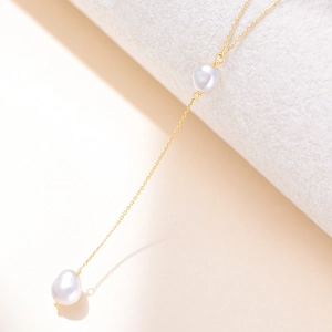 Elegante goldene Y-Halskette mit Barockperlen auf minimalistischem Steindisplay