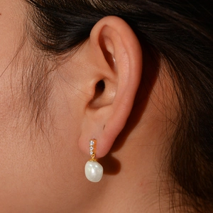 Detail of gold pearl earrings with three zircon stones worn by a model in a close-up view