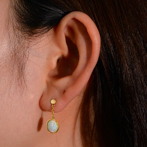 Detail of a gold-plated opal drop earring on a model showing elegant texture and size