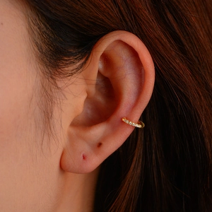 Gros plan d'un earcuff doré en forme de C serti de zircons sur l'oreille d'un modèle
