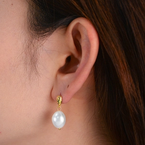 Detailed view of a Baroque pearl earring with textured gold-tone metal on a female ear