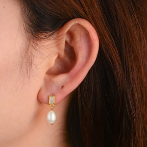 Boucles d'oreilles dorées avec zircon rectangulaire et perle goutte blanche sur modèle