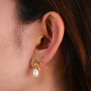 Close-up of golden bow stud earring with a white teardrop pearl worn by a model