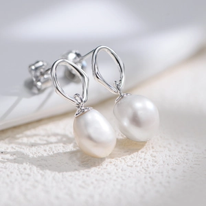 Macro shot of silver geometric earrings with lustrous white baroque pearls on white stone