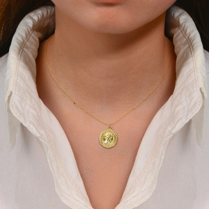Detail view of a vintage gold portrait coin pendant necklace on a white shirt