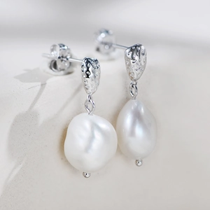 Detail of baroque pearl earrings with hammered silver texture on white stone