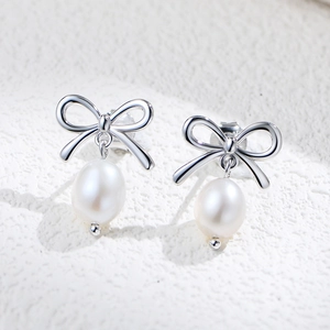 Elegant S925 silver bow stud earrings with natural freshwater pearls on stone texture