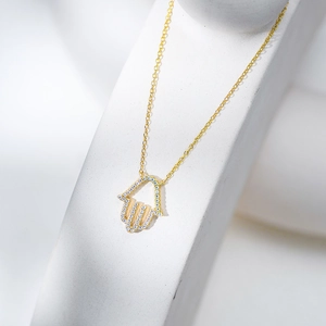 Detail der goldenen Hamsa-Halskette mit weißen Zirkonia auf minimalistischem Steinsockel
