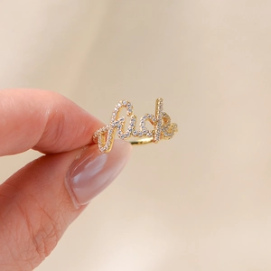 Détail macro d'une bague en argent S925 doré avec lettres cursives et incrustations de zircon