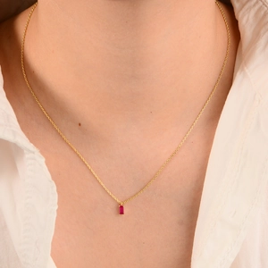 Elegant gold necklace with rectangular red zircon pendant on a female model