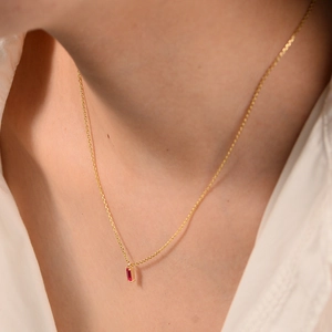 Close-up of elegant gold necklace featuring a rectangular red crystal pendant on neckline